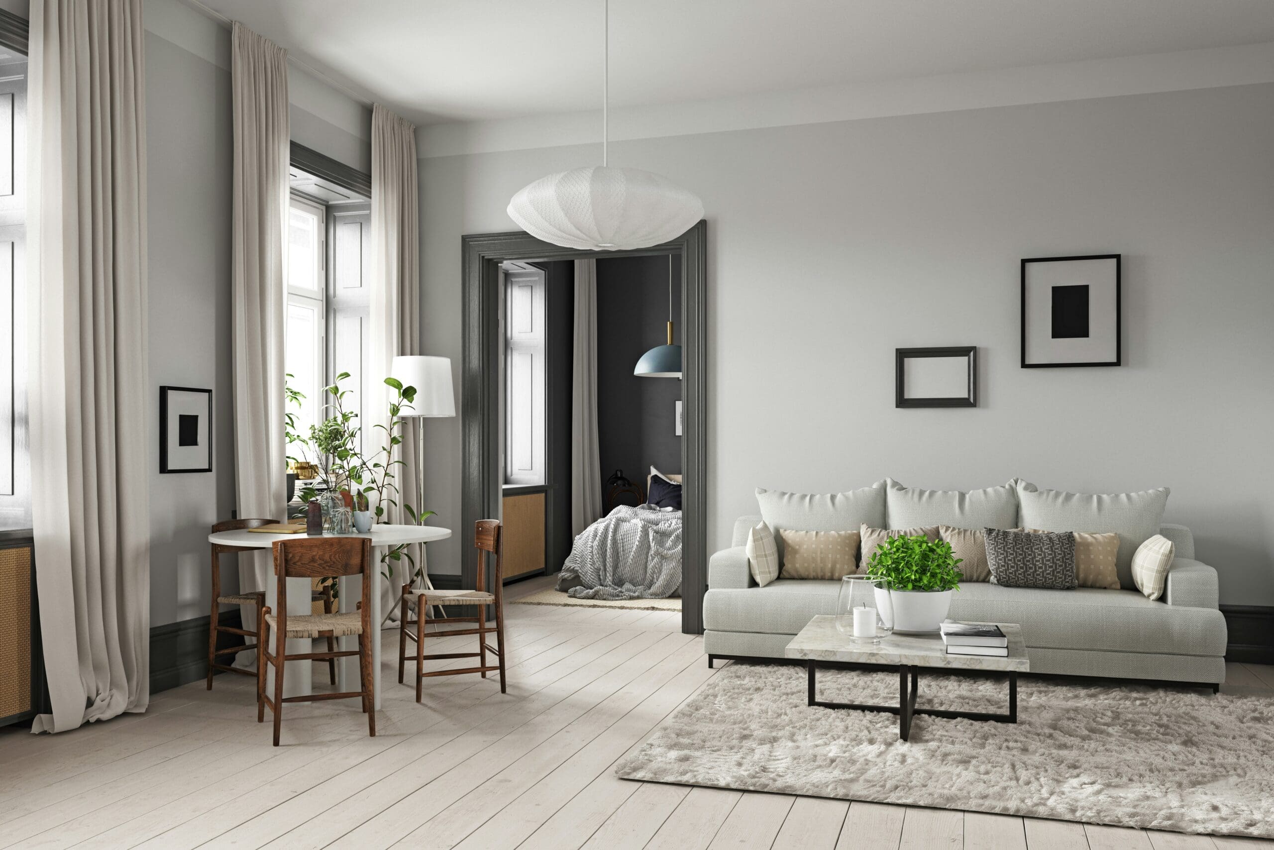 A modern living room with a minimalist design. It features a light gray sofa, a coffee table with a potted plant, a round dining table with two wooden chairs, and large windows with sheer curtains. The space is decorated with framed artwork and boasts carpets, including a large textured rug.