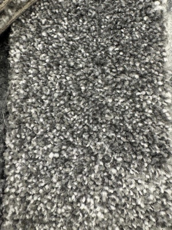 A close-up image of a grey and white textured fabric, showing a densely packed, plush and fluffy surface. The fibers appear uniform and soft, indicating a thick, carpet-like material.