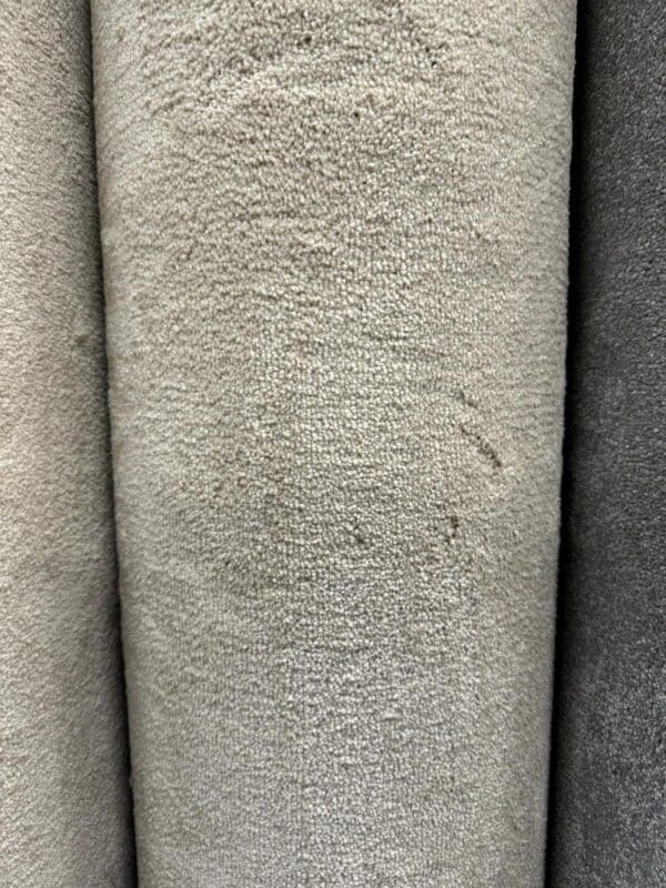 Close-up of three vertical rolls of the Enchantment 5x4m textured fabric in shades of light beige and grey, showcasing their soft yet slightly rough surfaces. The fabrics have a uniform texture and appear tightly rolled.