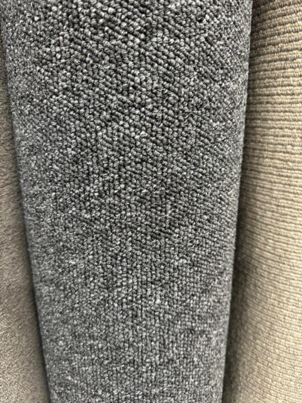 Close-up photo showcasing three rolls of the Gala Black 3.9x4m fabric in varying shades of grey and beige. The focus is on the textured, woven surfaces, highlighting the subtle variations in color and texture.