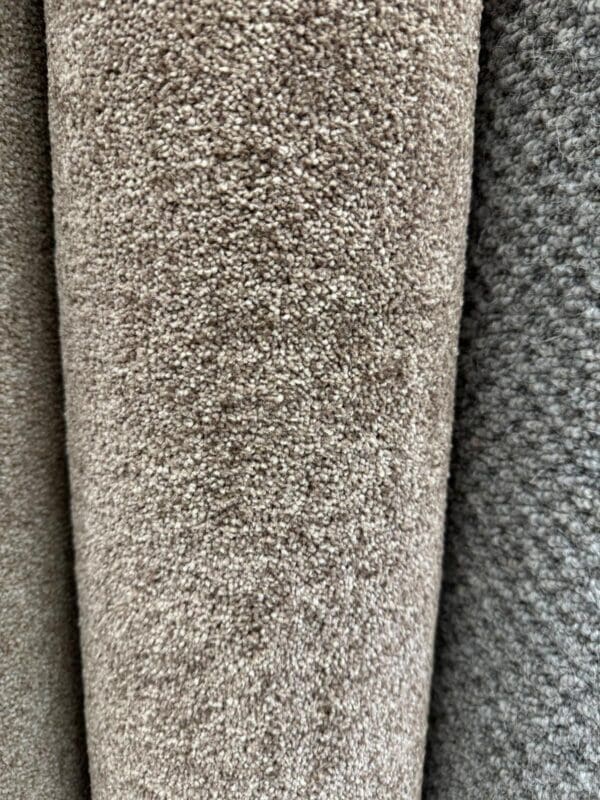 Close-up image of two rolled carpets, one in light beige and another in gray. The textures of both carpets are clearly visible, with the Senna Twist Brown 2x4m carpet having a looped texture and the gray carpet having a slightly coarser texture.