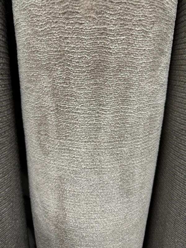 A close-up view of Winsor Pebble 2.3x4m, showcasing its light gray, textured fabric with a subtle horizontal pattern. The material appears soft and slightly reflective, making it suitable for upholstery or drapery applications.