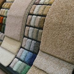 Close-up of a display showing various carpet samples in a store. The samples vary in color, including shades of beige, brown, blue, and green, neatly organized on curved stands.